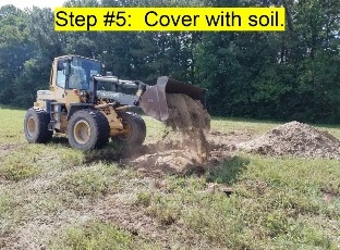 An Image of a payloader placing soil on top of the above ground burial trench.