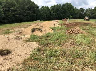 An Image multiple above ground burial trenches fully covered with soil. The soil is a mound over the trench approximately two feet high in the center.