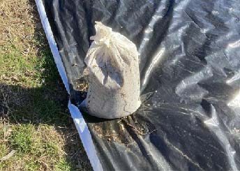 A picture containing an occultation silage tarp with a 10-15 lb. bag standing up on the edge of the tarp.